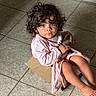 child, toddler, curly_hair, blue_eyes, portrait, sitting, cardboard, chair, pink_clothing, pajamas, indoor, tile_floor, barefoot, looking_at_camera, serious_expression, cute, fashion, home, photography