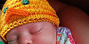 Loralie joined the competition — help win amazing prizes! baby, sleeping, hat, knitted_hat, yellow, chick_hat, pacifier, floral_outfit, colorful, infant, person, arm, closeup, cute, peaceful, resting, indoors, soft_light, portrait, child
