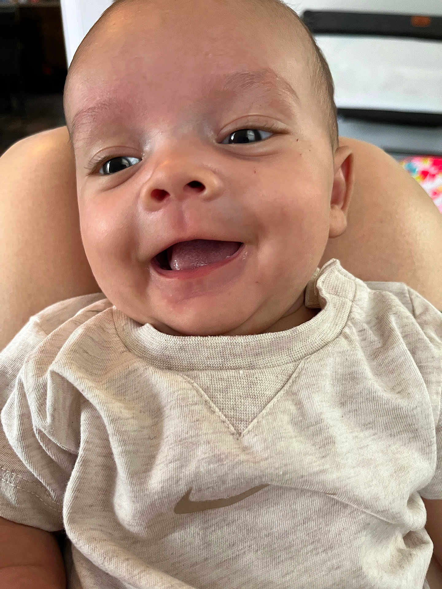 Roman is registered to the contest to win money with this photo: baby, smiling, close_up, infant, clothing, nike, person, face, happy, cute, skin, sitting, indoor, child, young, portrait, head, joy, casual, tshirt