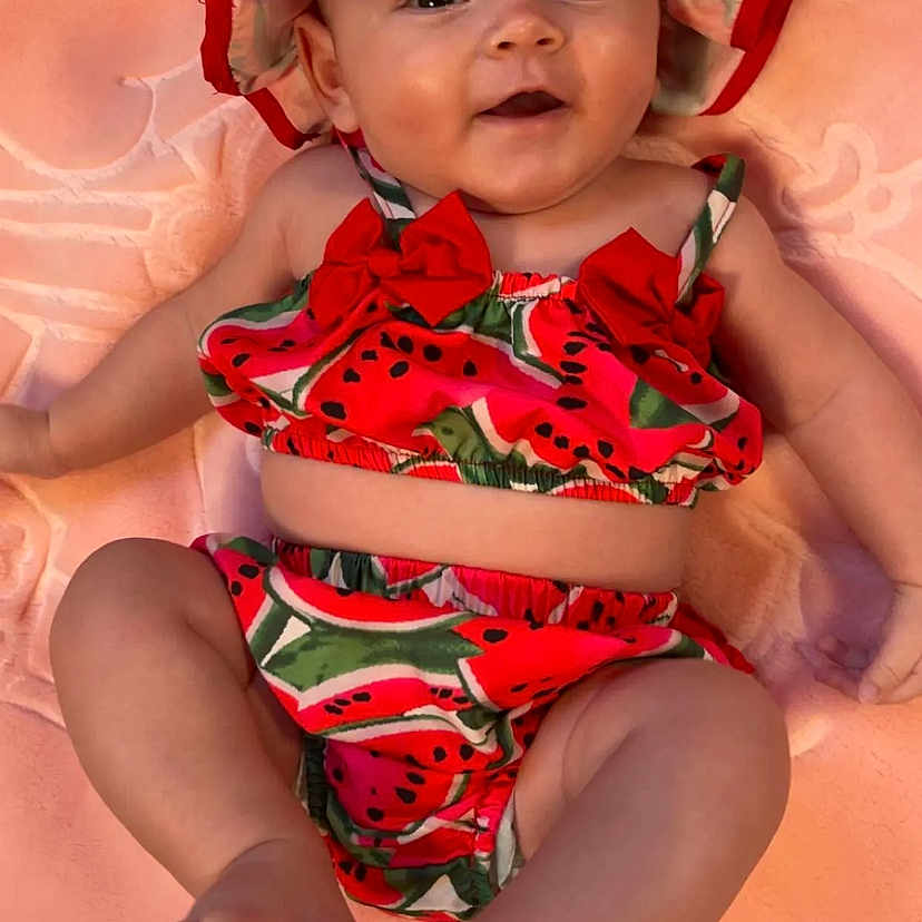 Joy participe au concours pour gagner de l'argent avec cette photo : adorable, baby, child, chubby_legs, closeup, cute, face, happy, hat, headwear, infant, lying_down, person, pink_blanket, playful, portrait, skin, smiling, summer_clothes, watermelon_outfit