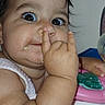 baby, child, face, finger, nose, food, snack, toys, activity_seat, curious, playful, wide_eyes, chubby_cheeks, indoor, person, expression, hand, baby_clothing, table, closeup