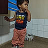 toddler, child, indoor, sneakers, oversized_shoes, pink_pants, blue_shirt, window, tiles, floor, standing, person, casual_clothing, young_child, curious_expression, hand_on_face, short_hair, home, daylight, cute