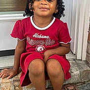 Niema joined the competition — help win amazing prizes! child, girl, smiling, curly_hair, bow, red_dress, black_shoes, doorstep, brick, welcome_mat, outdoor, portrait, happy, casual_clothing, sitting, cute, home, person, fashion, youth