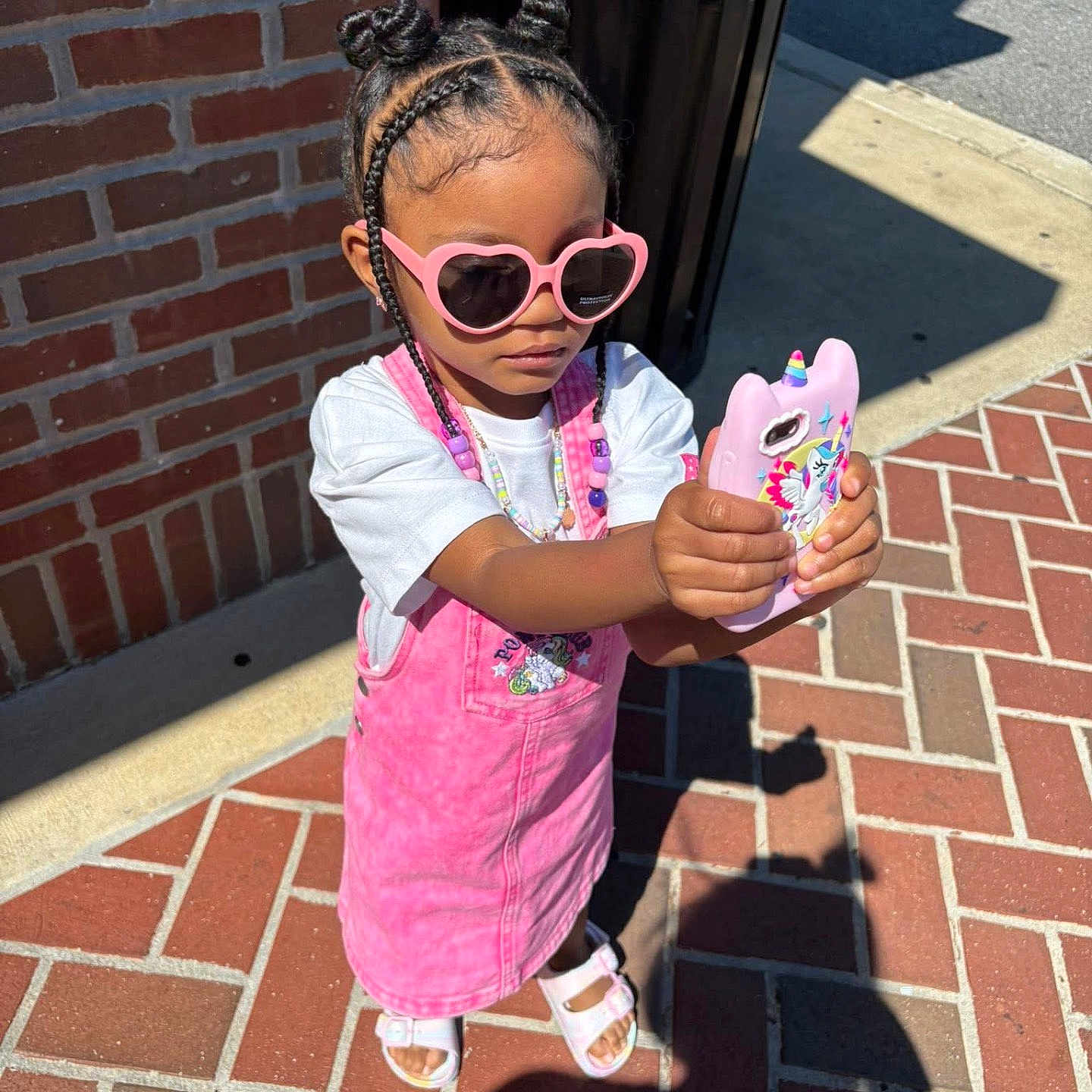 Niema is registered to the contest to win money with this photo: accessories, beads, braided_hair, brick_wall, casual, child, cute, fashion, girl, outdoor, pink_dress, portrait, sandals, shadow, sidewalk, standing, summer, sunglasses, sunny, unicorn_phone_case