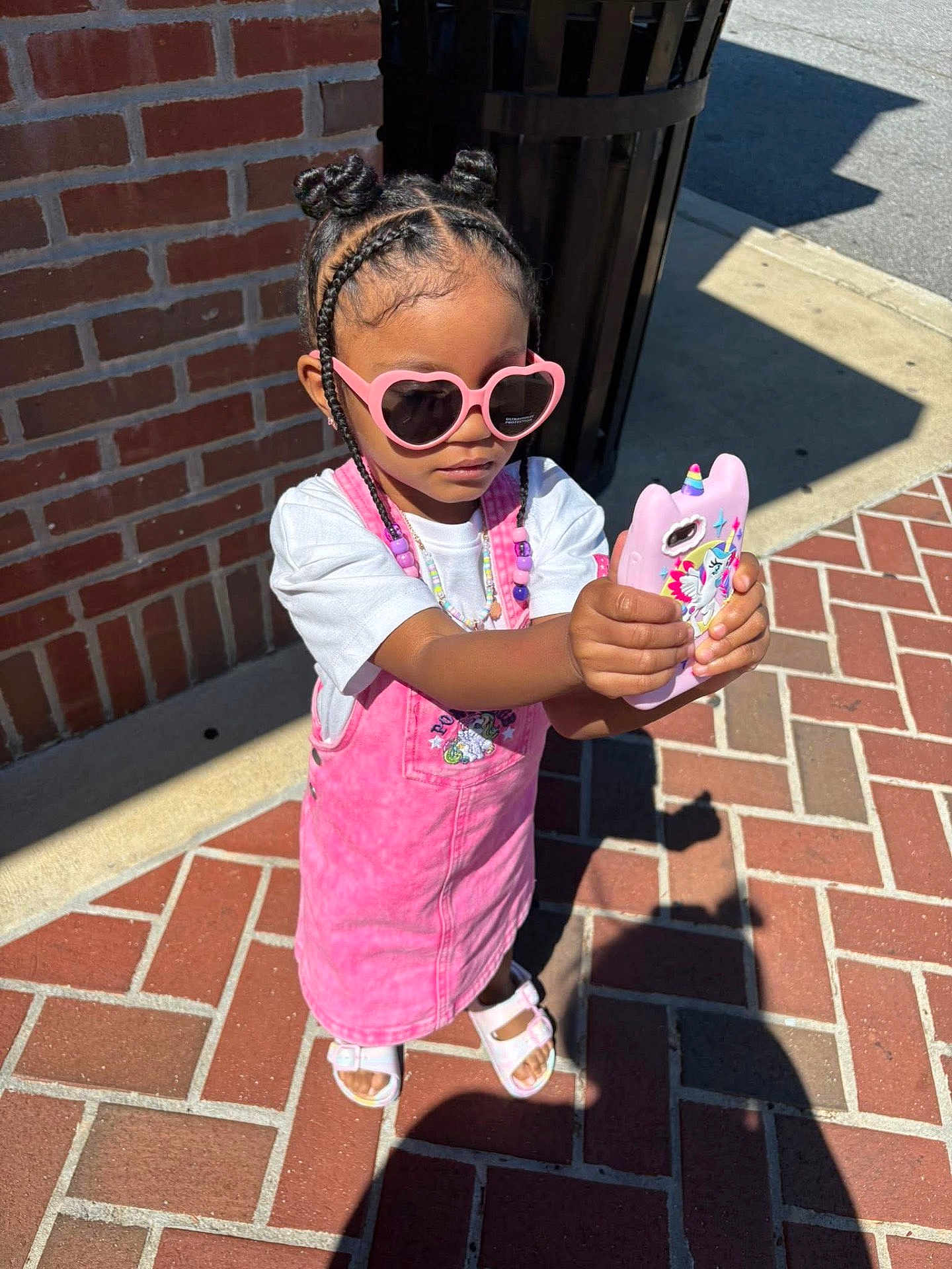 Niema is registered to the contest to win money with this photo: child, girl, sunglasses, pink_dress, braided_hair, unicorn_phone_case, sidewalk, brick_wall, sandals, sunny, outdoor, standing, fashion, accessories, beads, shadow, casual, cute, summer, portrait