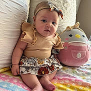 Bailey is registered to the contest to win money with this photo: baby, infant, child, headband, bow, skirt, ruffles, plush_toy, stuffed_animal, blanket, patterned_clothing, pastel_colors, sitting, indoors, cute, soft_lighting, chubby_cheeks, foot, hand, couch