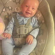 Theodore is registered to the contest to win money with this photo: baby, child, smile, blue_onesie, baby_seat, elephant_pattern, straps, cushion, infant, happy, indoors, seat_belt, baby_toys, soft_lighting, cute, portrait, comfort, young_child, sitting, face
