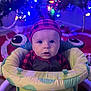 baby, infant, child, baby_seat, hat, plaid, red, black, christmas_lights, holiday, festive, indoor, face, expression, seated, colorful, soft_lighting, cute, warm, carpet
