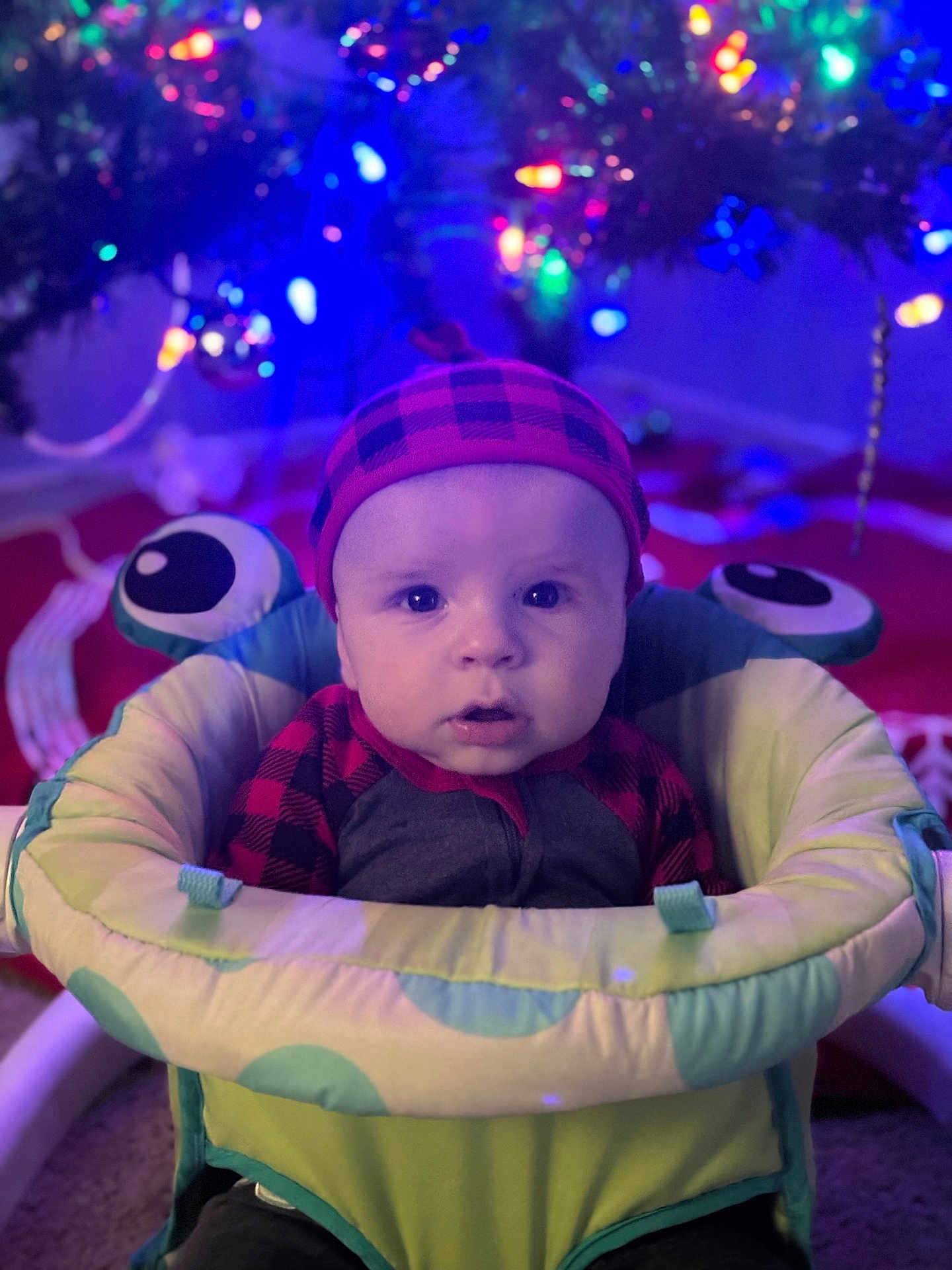 Jude is registered to the contest to win money with this photo: baby, infant, child, baby_seat, hat, plaid, red, black, christmas_lights, holiday, festive, indoor, face, expression, seated, colorful, soft_lighting, cute, warm, carpet