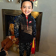 Andrew joined the competition — help win amazing prizes! child, smiling, portrait, standing, indoors, fireplace, holiday_decorations, bows, toys, suitcase, nike_clothing, sportswear, black_outfit, sneakers, red_accents, tile_floor, home, festive, happy, full_body