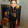 child, smiling, portrait, standing, indoors, fireplace, holiday_decorations, bows, toys, suitcase, nike_clothing, sportswear, black_outfit, sneakers, red_accents, tile_floor, home, festive, happy, full_body