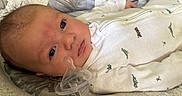Paul joined the competition — help win amazing prizes! baby, bed, child, closeup, clothing, cushion, dinosaur_print, eyes, face, hand, indoor, infant, newborn, onesie, pacifier, pattern, portrait, skin, sleeping_area, soft_toys