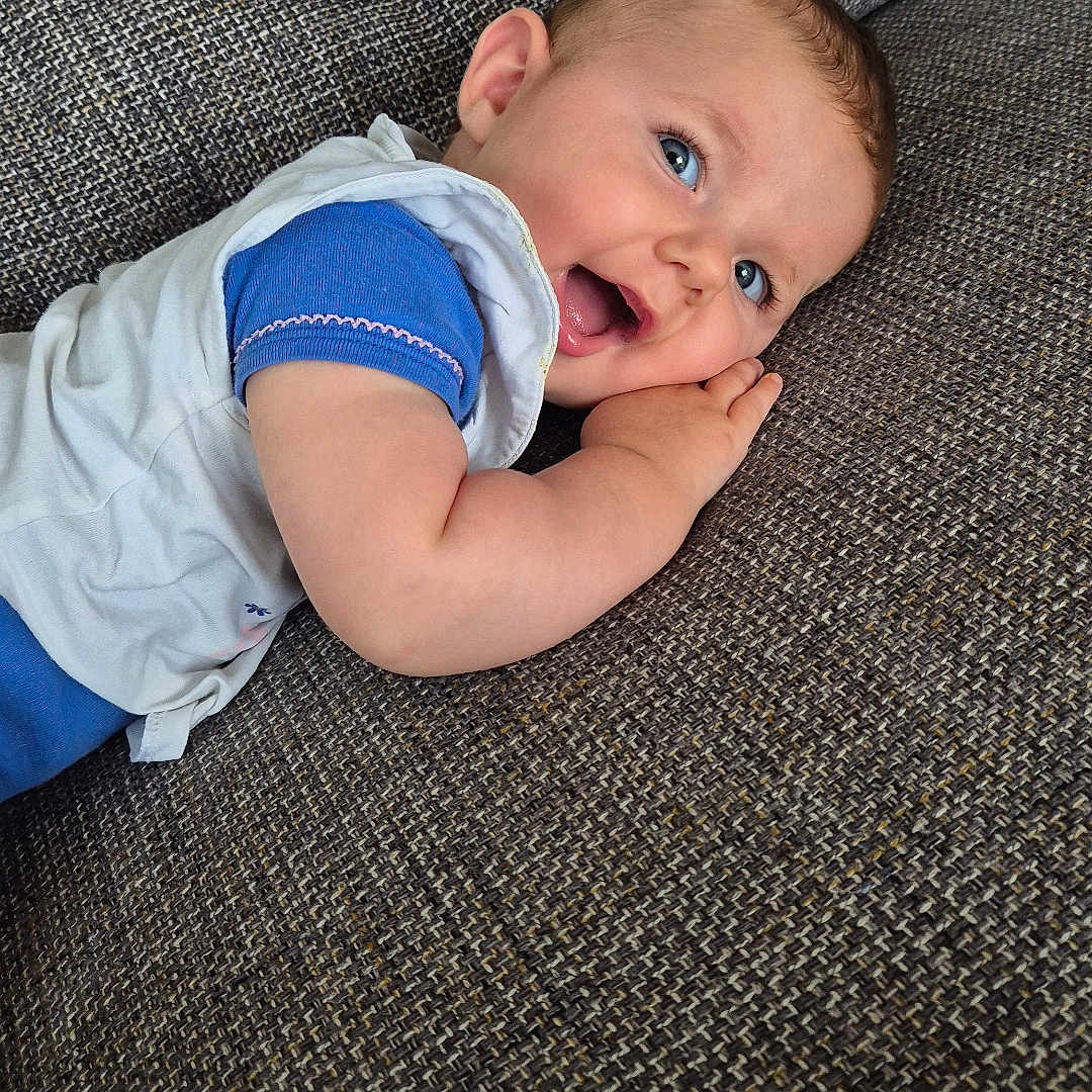 Aimée a rejoint le concours — aidez-le/la à gagner de superbes lots ! baby, blue_eyes, casual_clothing, child, close_up, couch, cute, face, hand, happy, indoor, infant, lying_down, portrait, relaxing, skin, smiling, textured_fabric, toddler, young_child