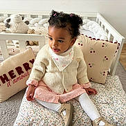 Ambre participe au concours pour gagner de l'argent avec cette photo : toddler, child, baby, curly_hair, pink_dress, cardigan, white_tights, beige_shoes, cushion, crib, stuffed_toy, pillow, nursery, floor, carpet, indoor, portrait, cute, seated, curious