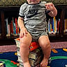 baby, child, toddler, portrait, sitting, books, book_stack, bookshelf, reading, indoor, home, playroom, alphabet_blocks, toy_blocks, colorful_rug, carpet, nike_shirt, onesie, barefoot, serious_expression