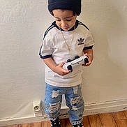 Randiell participe au concours pour gagner de l'argent avec cette photo : toddler, child, indoor, beanie, black_hat, white_shirt, adidas, ripped_jeans, blue_jeans, black_sneakers, game_controller, wooden_floor, wall, standing, looking_down, casual_clothing, floor_rug, necklace, pom_pom, young_child