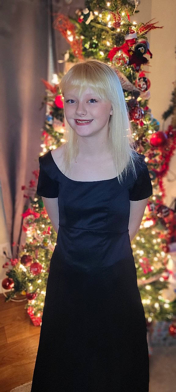 Isabella is registered to the contest to win money with this photo: christmas_ornament, christmas_tree, dress, facial_expression, hair, hairstyle, happy, head, holiday_ornament, joy, light, outerwear, person, photograph, plant, red, sleeve, smile, standing, tree