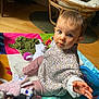 baby, child, play_mat, toy, indoor, floor, curious, blue_eyes, hand, pink_pants, patterned_shirt, plush_toy, pacifier, wooden_floor, chair, colorful, soft_toys, cushion, expression, person