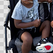 Jordyn Evans joined the competition — help win amazing prizes! child, stroller, sneakers, grey_shirt, black_shorts, footwear, puzzled_expression, young_boy, sitting, outdoor, person, toy, plastic_cup, hand, curly_hair, casual_clothing, baby_stroller, legs, black_shoes, transparent_background