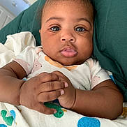 Amirah is registered to the contest to win money with this photo: baby, infant, child, hands, blanket, bird_pattern, cushion, green, clothing, face, portrait, skin, eyes, fingers, home, interior, comfort, cute, relaxed, lying_down