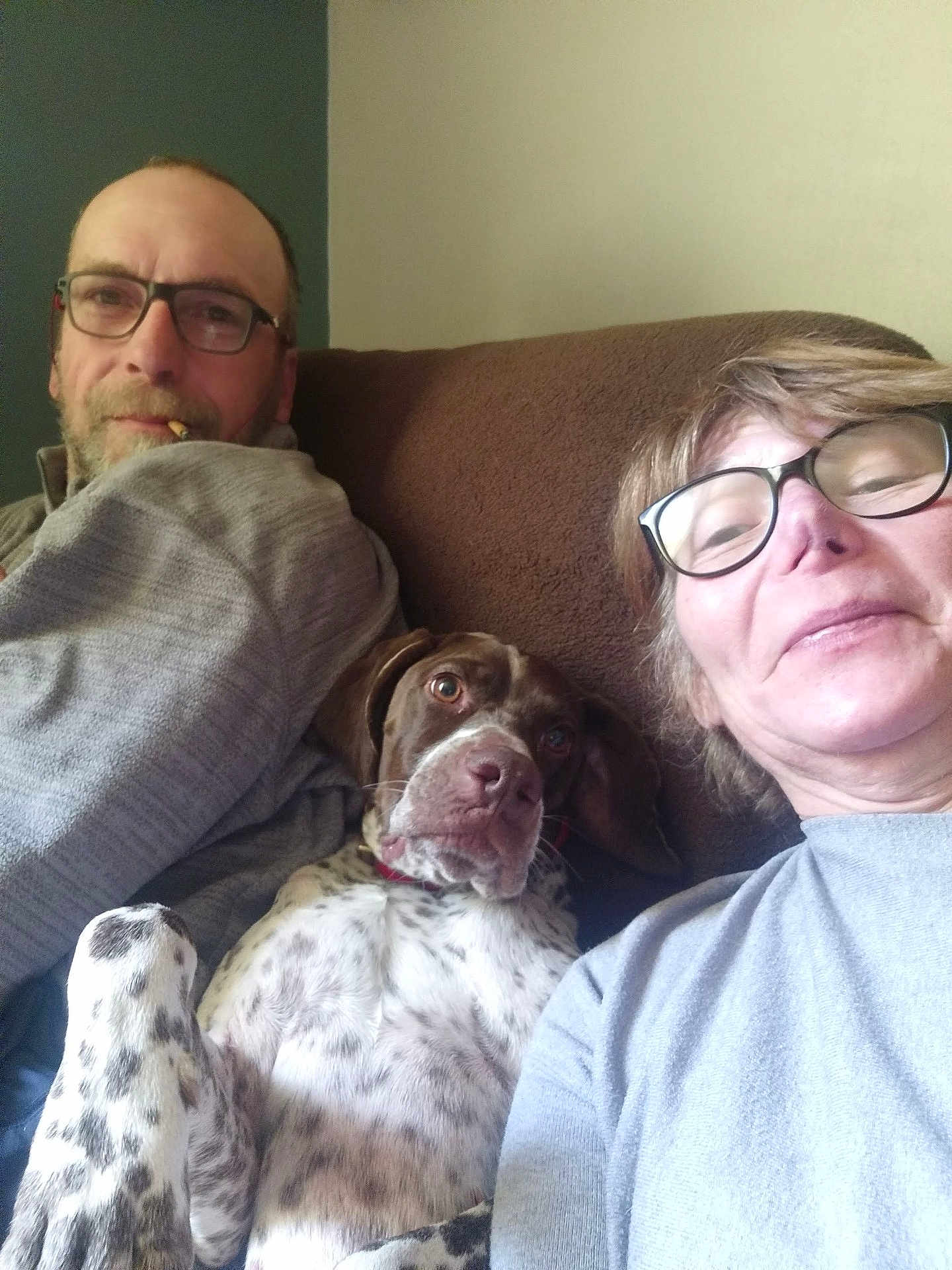 Rodja participe au concours pour gagner de l'argent avec cette photo : man, woman, dog, glasses, couch, indoor, casual, pet, brown_couch, spotted_dog, relaxed, smile, beard, short_hair, sweater, portrait, home, comfort, cigarette, selfie
