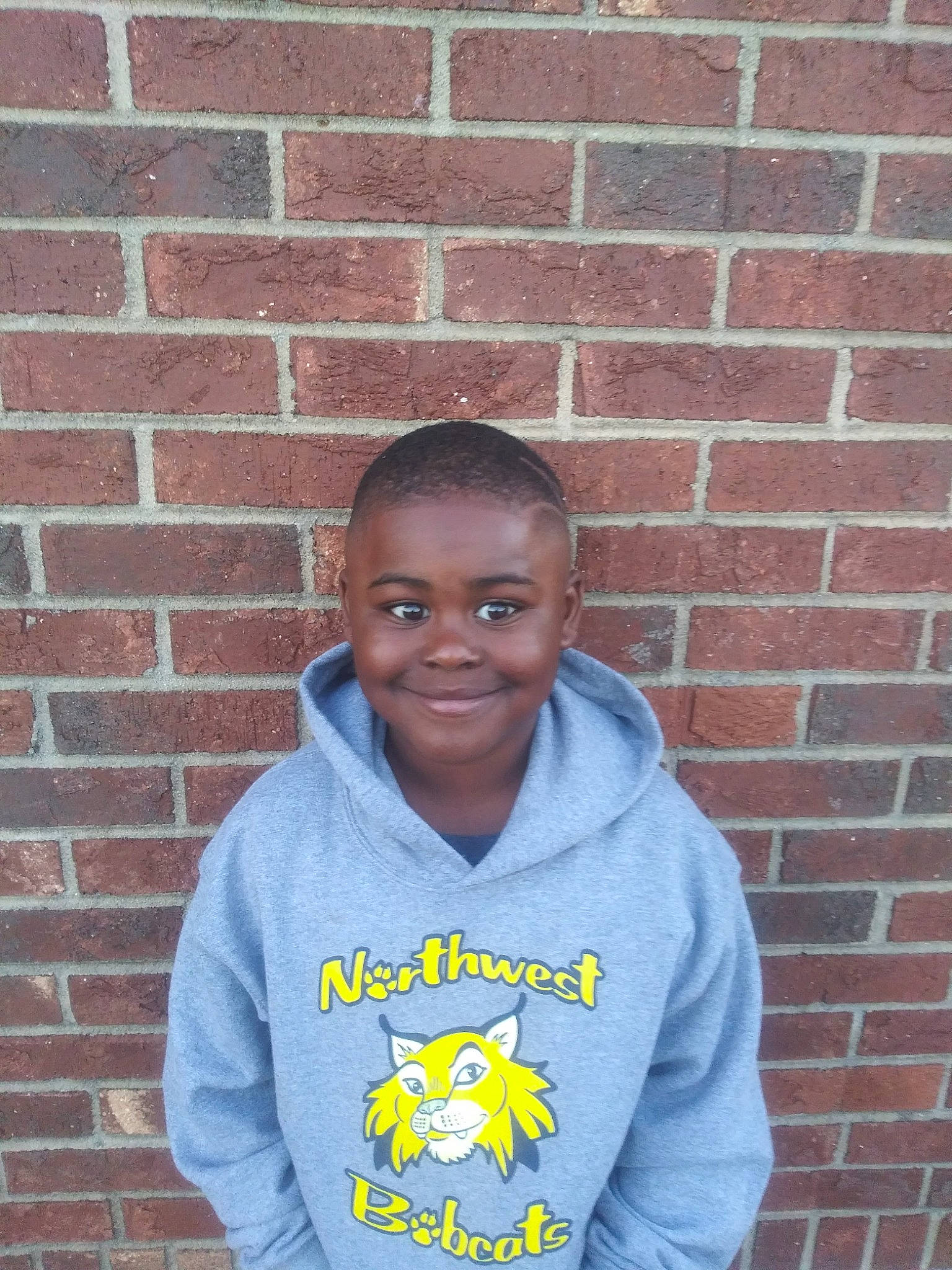 Anthony is registered to the contest to win money with this photo: brick, brickwork, buzz_cut, chin, electric_blue, face, forehead, grey, happy, head, hoodie, jersey, joy, mouth, organ, person, photograph, sleeve, smile, sportswear