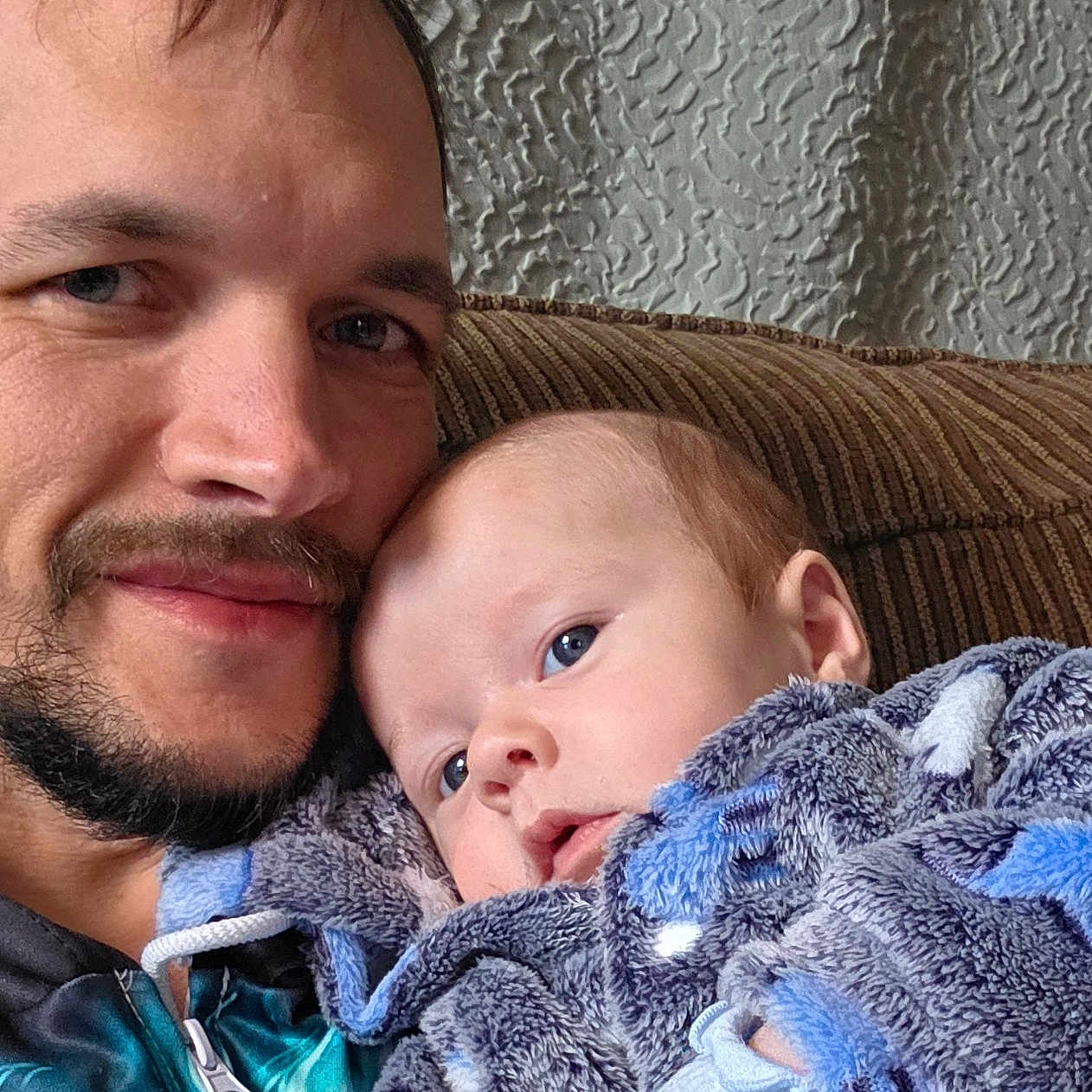 Eiron joined the competition — help win amazing prizes! adult, baby, beard, blanket, blue_eyes, closeup, couch, cozy, face, hooded_blanket, indoor, infant, man, parent_child, plush, portrait, smile, sofa, striped_fabric, textured_wall