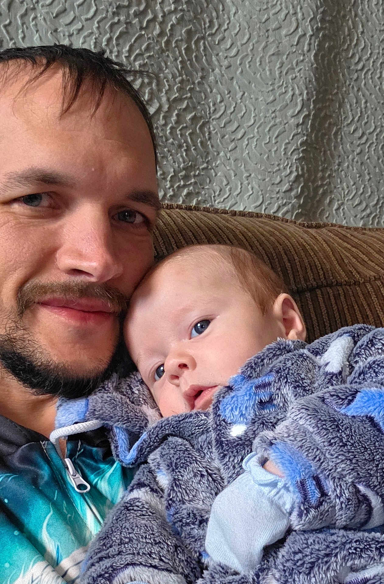 Eiron joined the competition — help win amazing prizes! baby, infant, man, adult, beard, couch, sofa, blanket, hooded_blanket, blue_eyes, portrait, closeup, smile, face, striped_fabric, textured_wall, indoor, cozy, parent_child, plush