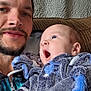 Eiron is registered to the contest to win money with this photo: baby, man, father, infant, selfie, sofa, couch, blanket, fuzzy_clothing, mittens, beard, portrait, indoor, textured_wall, blue, eyes, smile, closeup, parent_child, cozy