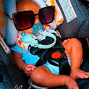 Trez Jhur joined the competition — help win amazing prizes! baby, infant, car_seat, sunglasses, pacifier, buckled, child, portrait, seated, floral_pattern, toy, travel, vehicle, safety_harness, blue_clothing, legs, feet, indoor, funny, photography