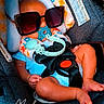 baby, infant, car_seat, sunglasses, pacifier, buckled, child, portrait, seated, floral_pattern, toy, travel, vehicle, safety_harness, blue_clothing, legs, feet, indoor, funny, photography