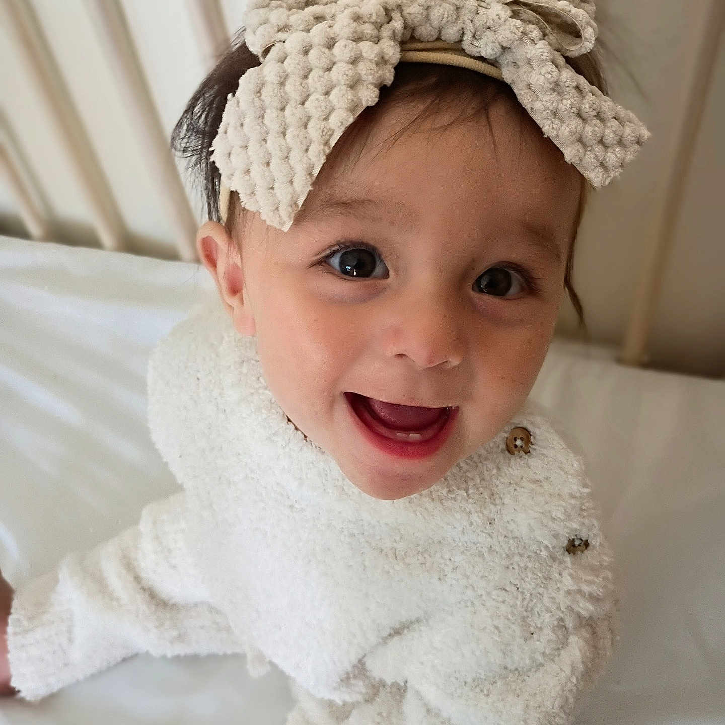 Athena Melody is registered to the contest to win money with this photo: baby, infant, child, portrait, smiling, happy, wide_eyes, bow_headband, white_outfit, cozy, bed, indoors, closeup, face, person, crawling, soft_texture, warm_lighting, cute, family_photo