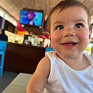 Enzo joined the competition — help win amazing prizes! toddler, child, smiling, face, indoor, white_tank_top, happy, person, cheeky, eyes, skin, hair, table, furniture, television, blurred_background, colorful, expression, portrait, candid