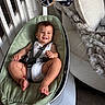 baby, smile, baby_rocker, harness, toy, hanging_toys, indoor, chair, blanket, furniture, floor, wood_floor, person, infant, happy, clothing, foot, hand, head, face