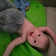 Theodore is registered to the contest to win money with this photo: arm, baby, child, childhood, cozy, cute, face, green_blanket, happy, head, indoor, infant, lying_down, plush_toy, portrait, skin, smiling, soft, stuffed_animal, toy