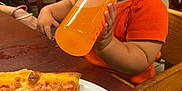 Jahkari joined the competition — help win amazing prizes! toddler, child, baby_bottle, orange_shirt, pizza, pepperoni, plate, wooden_table, wooden_chair, indoor, dining_area, food, drink, person, cute, young_child, seated, curious, restaurant, casual