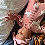 baby, infant, pink_onesie, headband, blanket, bed, hand, face, cute, sleepwear, child, lying_down, cozy, soft_fabric, pattern, indoor, newborn, person, reaching_hand, resting