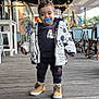 toddler, child, pacifier, jacket, mickey_mouse, outdoor, deck, wooden_floor, string_lights, cafe, chairs, tables, boots, clothing, smile, person, standing, casual, daylight, cute