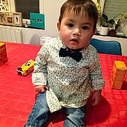 Oscar participe au concours pour gagner de l'argent avec cette photo : toddler, child, boy, indoor, table, red_tablecloth, shirt, bow_tie, jeans, striped_socks, face, curious, sitting, home, plant, photograph_frame, chair, window, cup, snack_box