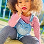Maya a rejoint le concours — aidez-le/la à gagner de superbes lots ! child, girl, curly_hair, bow, pink_shirt, denim_overalls, gray_tights, outdoor, sunlight, portrait, smile, face, hand, sitting, playful, casual_clothing, daylight, young, person, colorful