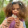 casual_clothing, child, closeup, curious, curly_hair, cute, dandelion, fall, flower, greenery, hair_clips, hands, jacket, nature, outdoor, pink_shirt, playing, portrait, soft_light, young_girl