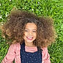 Maya a rejoint le concours — aidez-le/la à gagner de superbes lots ! child, smiling, afro_hair, grass, flowers, outdoor, greenery, happy, face, person, nature, casual_clothing, pink_shirt, blue_overall, portrait, young, relaxed, daylight, grass_field, childhood