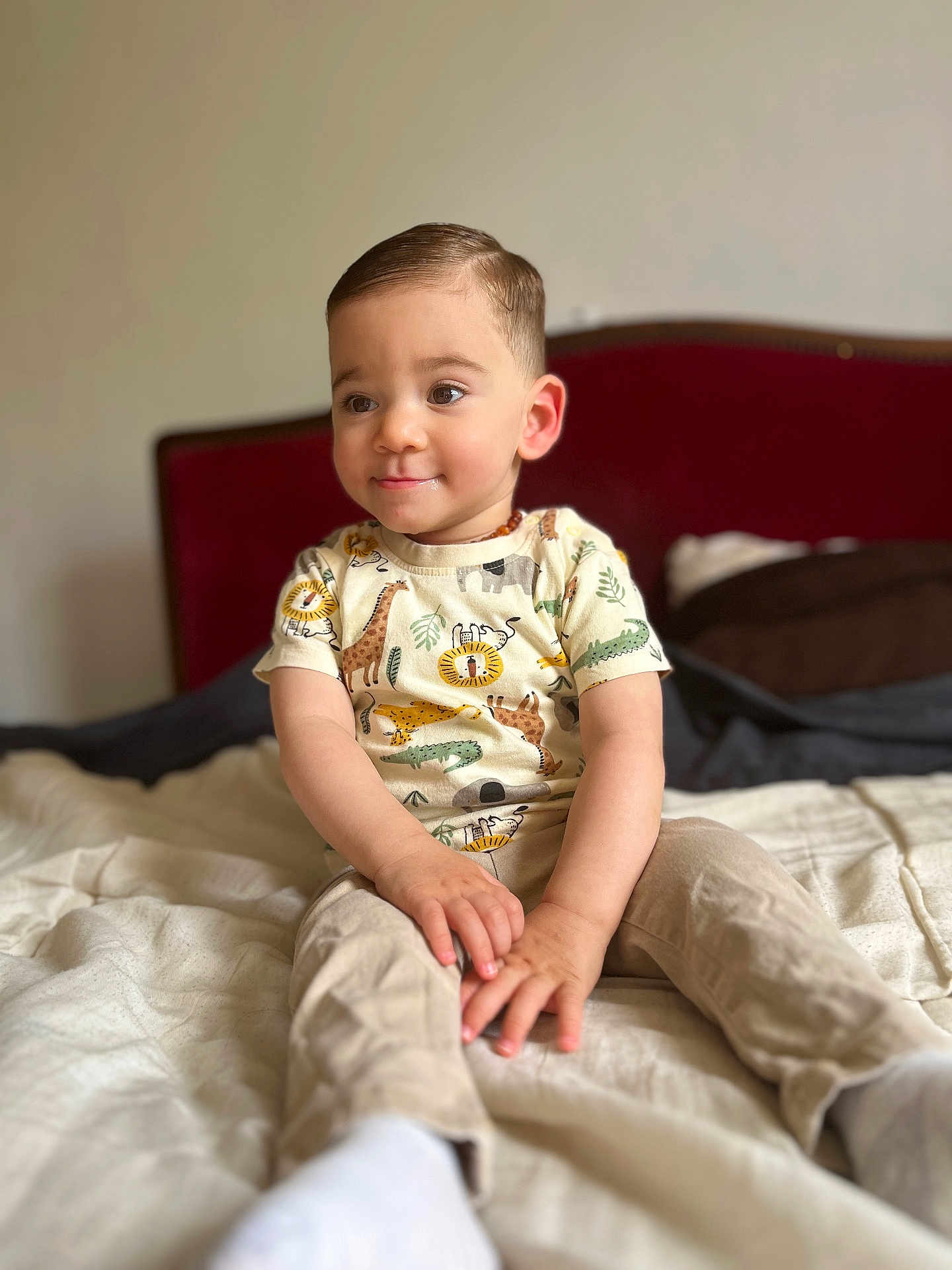 Ilham participe au concours pour gagner de l'argent avec cette photo : toddler, child, bed, clothing, animal_print, shirt, pants, sitting, smile, face, hair, indoors, furniture, blanket, comfort, cute, young_child, portrait, cozy, natural_light