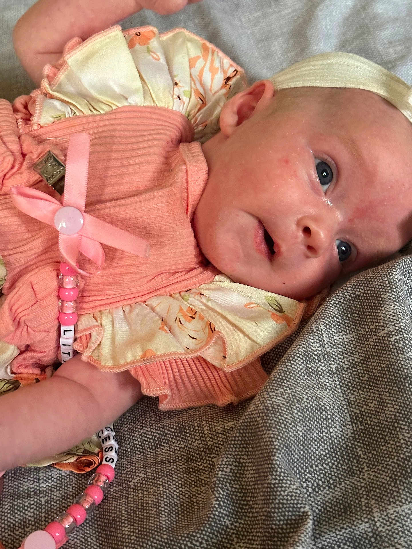 Freya is registered to the contest to win money with this photo: baby, infant, face, headband, clothing, fabric, beads, pacifier_clip, closeup, skin, person, child, lying_down, pink, texture, cute, newborn, soft_lighting, apparel, resting