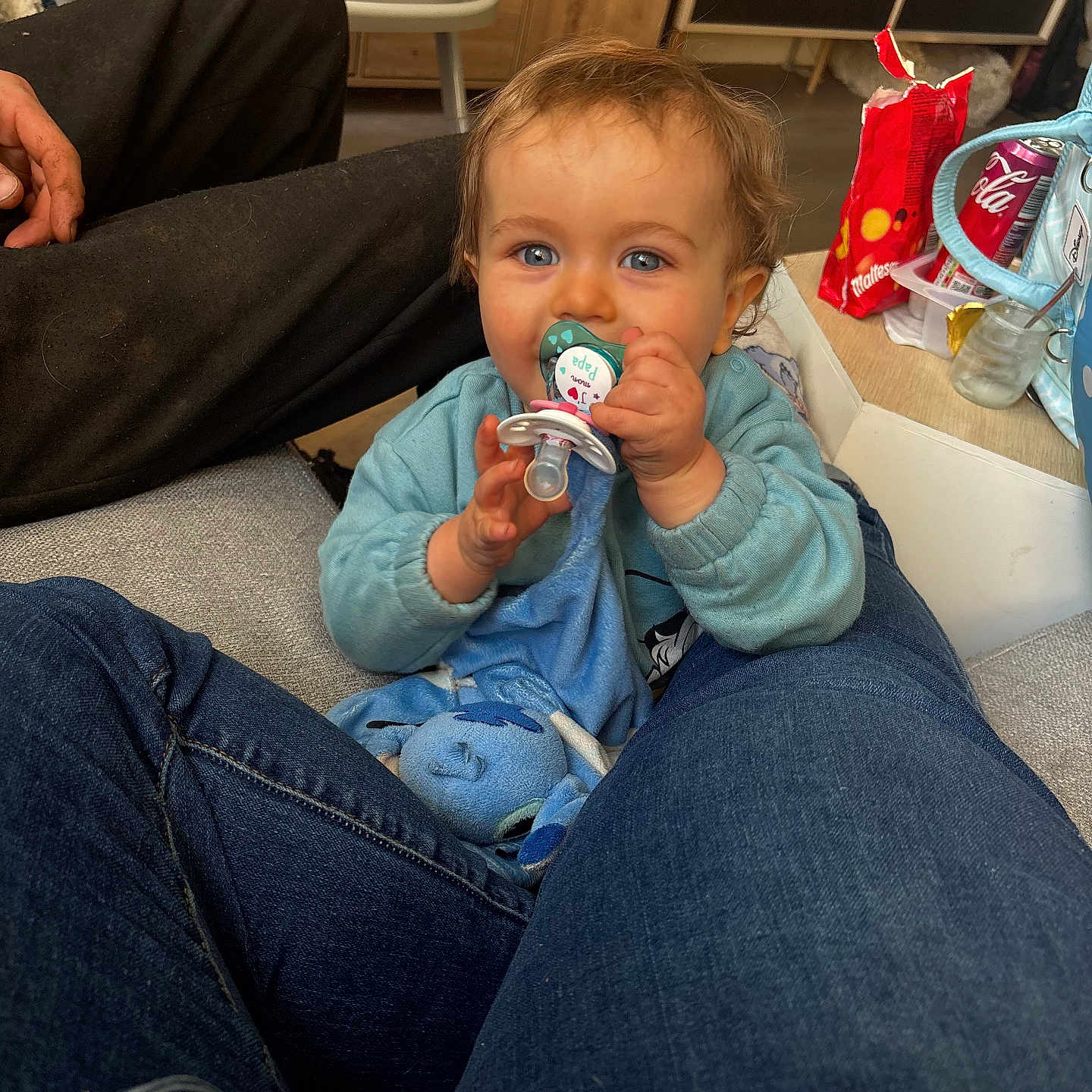 Naëlyo participe au concours pour gagner de l'argent avec cette photo : baby, blue_eyes, candid, casual, child, clothing, comfort, floor, furniture, hand, home, indoor, jeans, pacifier, person, plush_toy, seated, snacks, soda_can, wood