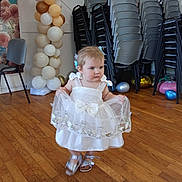Hannaya a rejoint le concours — aidez-le/la à gagner de superbes lots ! toddler, child, dress, white_dress, balloons, wooden_floor, party, celebration, chairs, stacked_chairs, indoor, person, footwear, sandals, floor, wall, decorations, baby, cute, movement