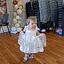toddler, child, dress, white_dress, balloons, wooden_floor, party, celebration, chairs, stacked_chairs, indoor, person, footwear, sandals, floor, wall, decorations, baby, cute, movement