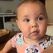 Briar Rose is registered to the contest to win money with this photo: baby, child, infant, portrait, face, indoors, home, curious, expression, eyes, short_hair, earrings, clothing, cartoon_print, colorful, furniture, shelves, television, table, photography