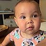 baby, child, infant, portrait, face, indoors, home, curious, expression, eyes, short_hair, earrings, clothing, cartoon_print, colorful, furniture, shelves, television, table, photography