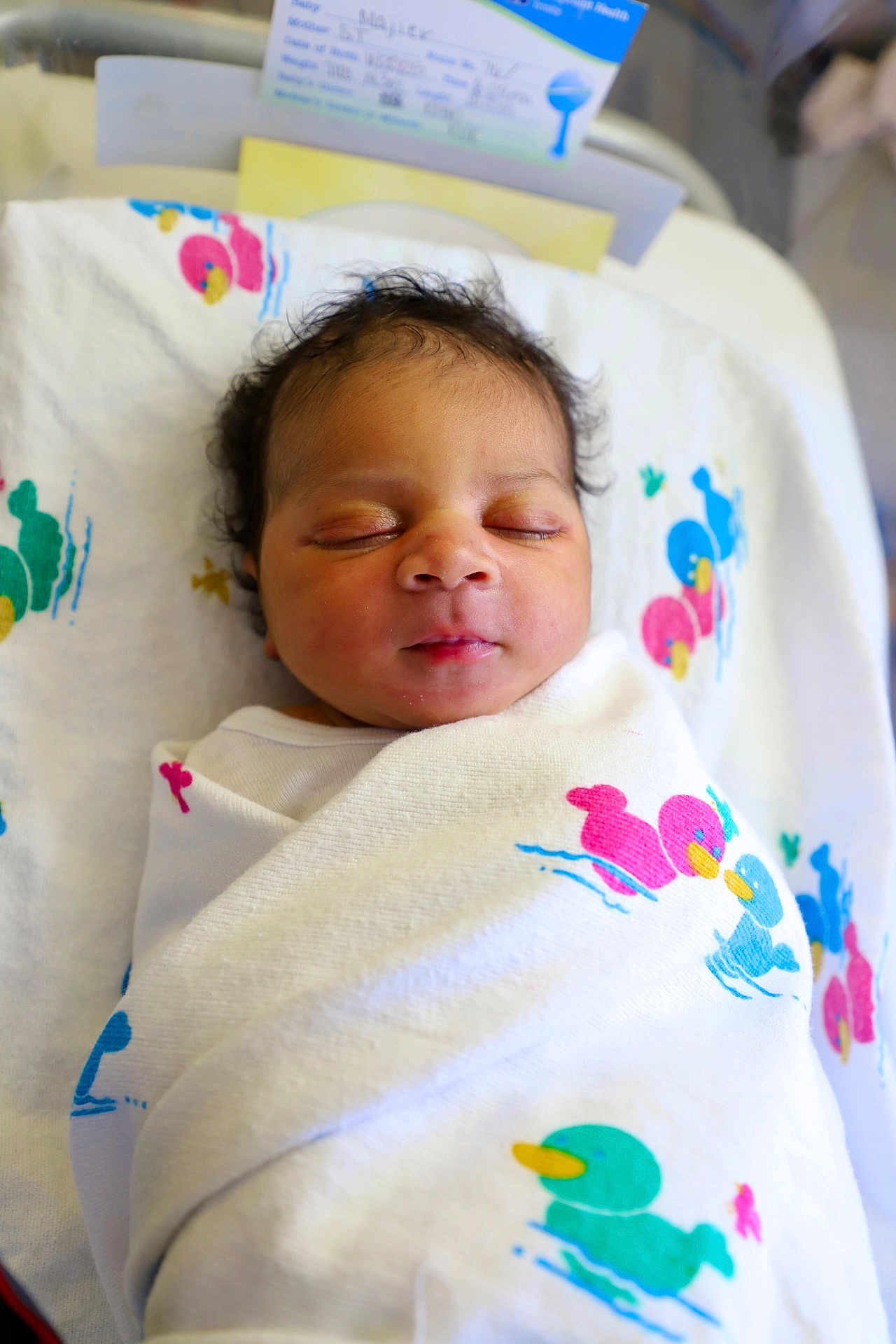 Majier is registered to the contest to win money with this photo: newborn, baby, sleeping, swaddled, blanket, duck_pattern, hospital_bassinet, infant, closeup, face, peaceful, curly_hair, soft_light, indoors, child, cute, resting, portrait, wrapped, toddler